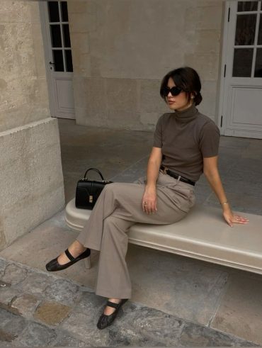 Mulher branca usando óculos de sol preto, blusa de tricô com gola, calça de alfaiataria e sapatilha de bailarina preta