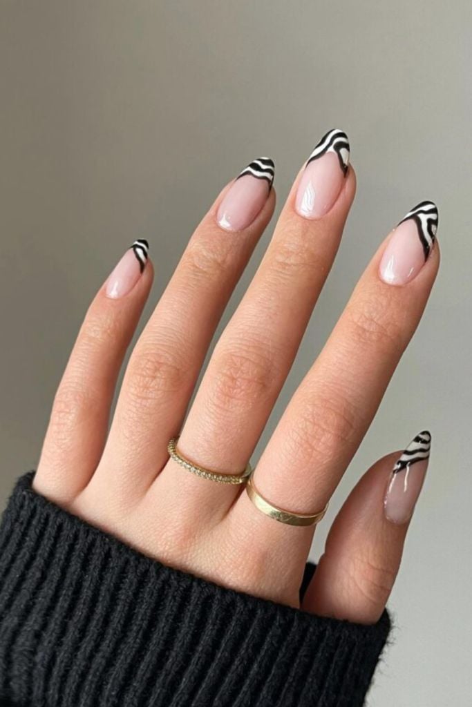 Mão branca com manga preta, anéis e unha amendoada com francesinha zebrada