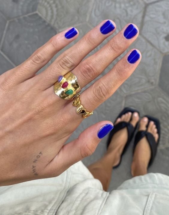 Mão branca com anéis e unha curta azul klein