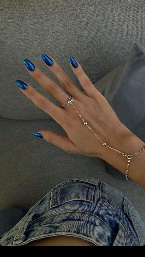Mão branca com unha azul cromada e acessório