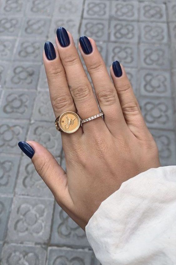 Mão branca com manga branca, anéis e unha azul profundo