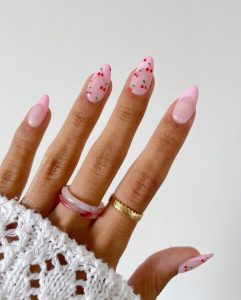 Mão branca com manga de renda, anéis e unha rosada com decoração de cereja