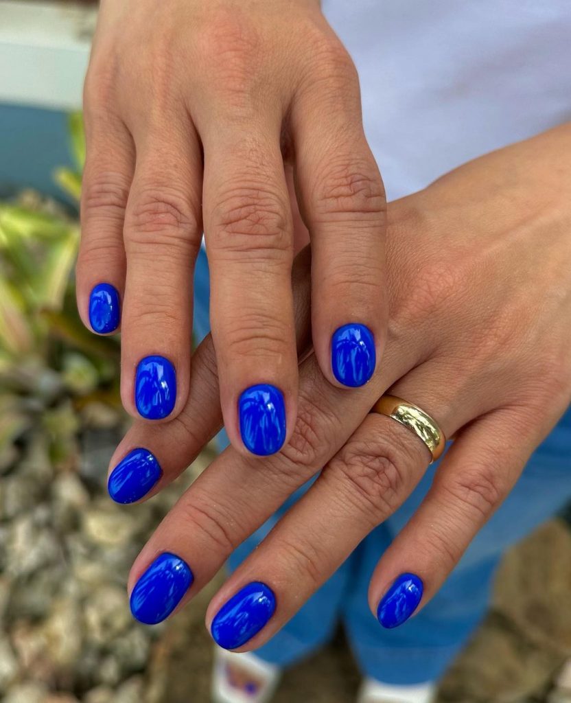 Mãos sobrepostas com anel e unha curta azul royal