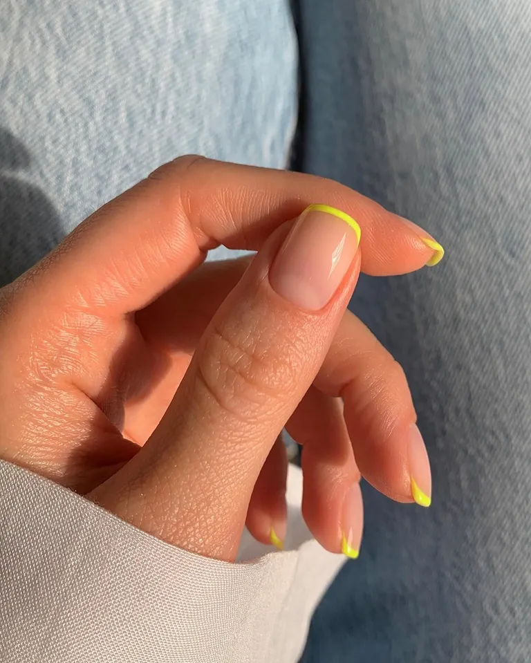 Mão branca com polegar em evidência com microfrancesinha amarela