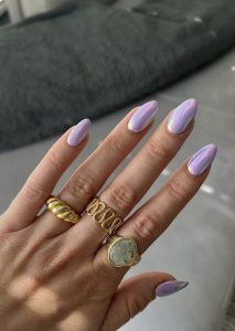 Mão branca com anéis e unha lilás metalizada