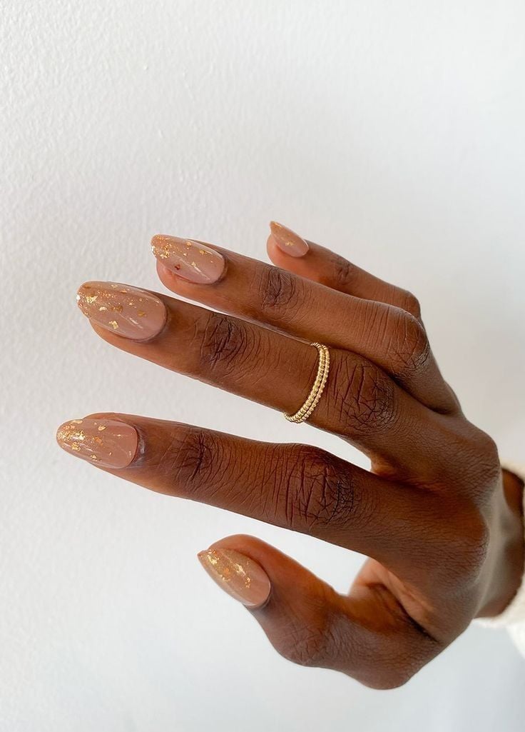 Mão negra com anéis curvada com unha nude com dourado