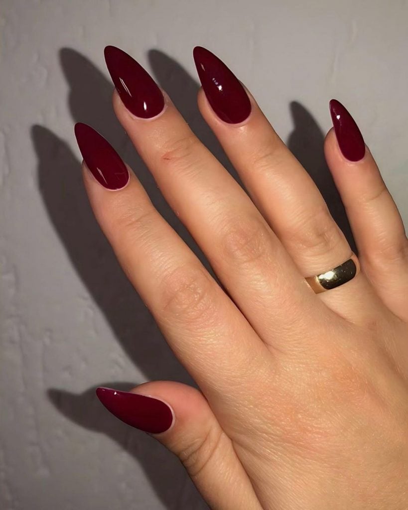 Mão branca com anel e unha stiletto vermelho cereja