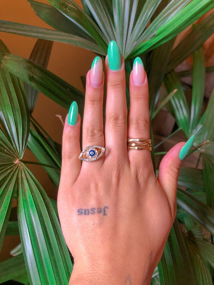 Mão branca com anéis e tatuagem, e unha verde água com francesinha lateral