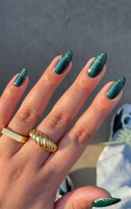 Mão branca com anéis dourados e unha verde esmeralda, com francesinha brilhosa
