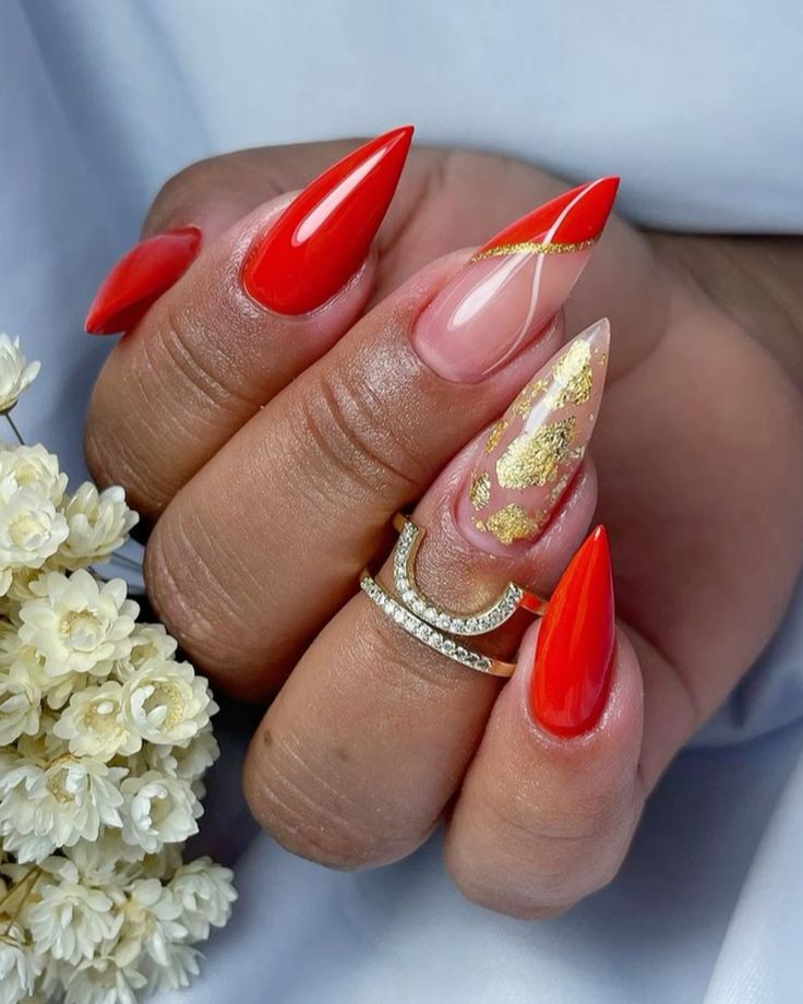 Mão curvada com anel e unha stiletto vermelha com folhas de ouro