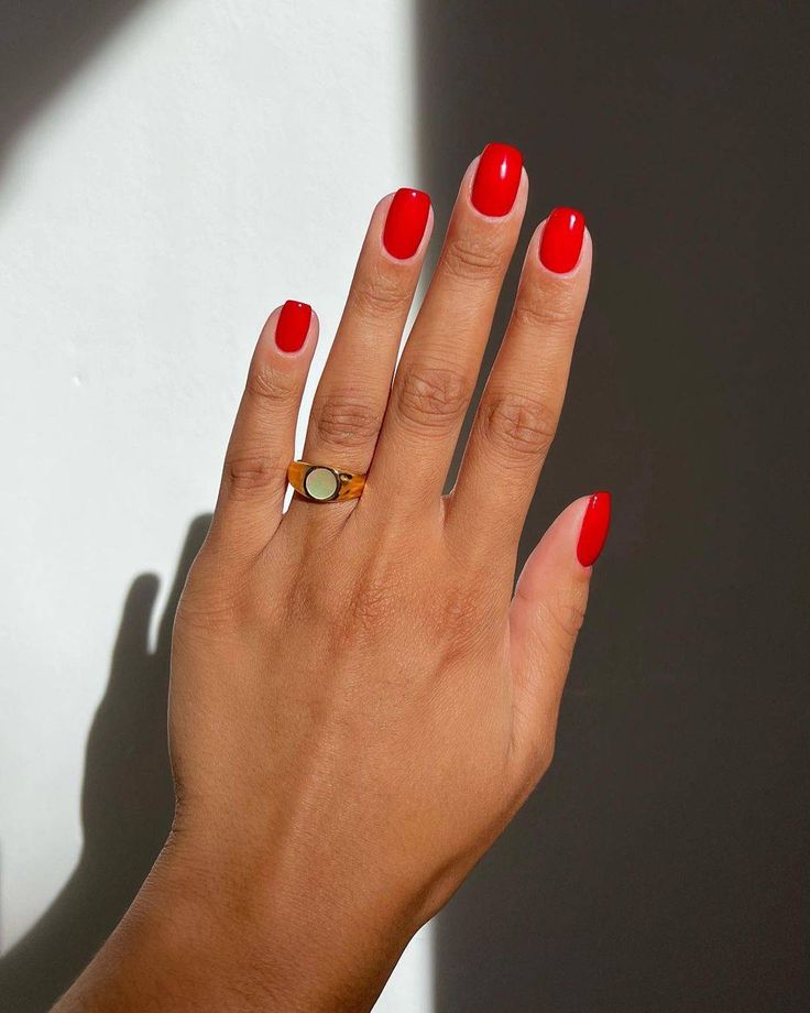 Mão branca com anel e unha curta vermelho vibrante