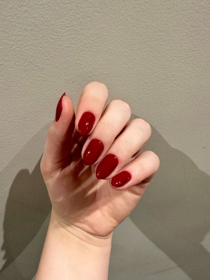 Mão branca curvada com unha amendoada vermelho vinho