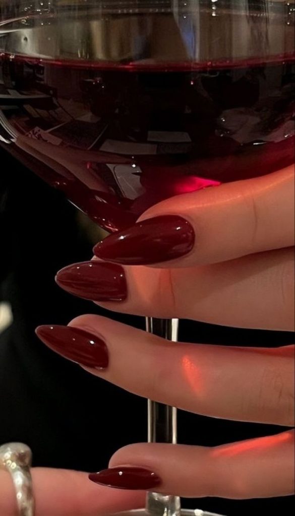 Mão branca segurando a taça com a unha stiletto vinho