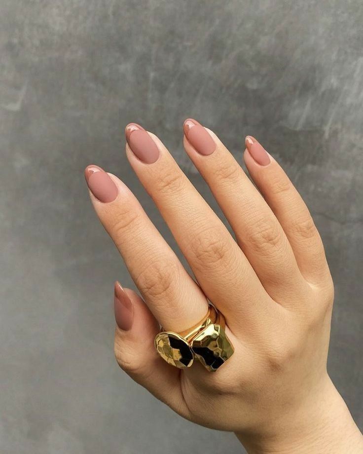Mão branca curvada com anel dourado e unha nude com francesinha