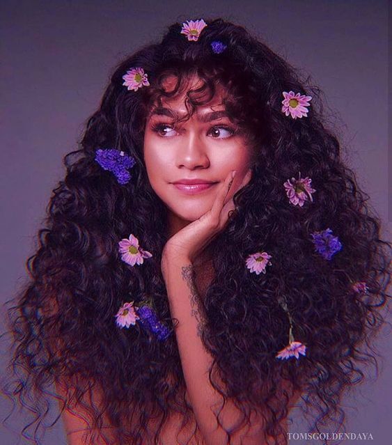 Zendaya com cabelo cacheado escuros e flores no comprimento