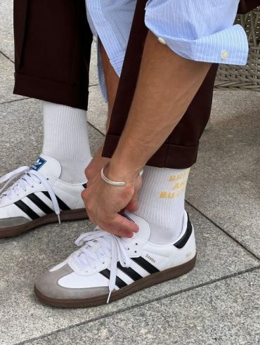 Foto de perna com calça marrom, meia branca e Adidas Samba