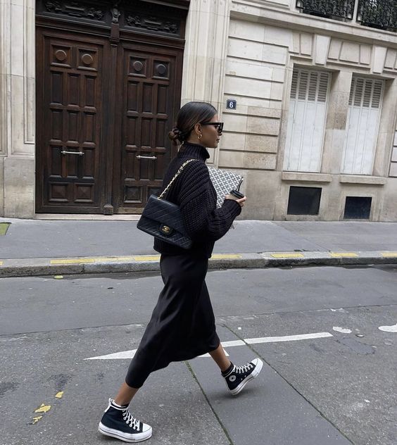 Mulher caminhando usando moletom preto e saia de cetim preta com all star preto