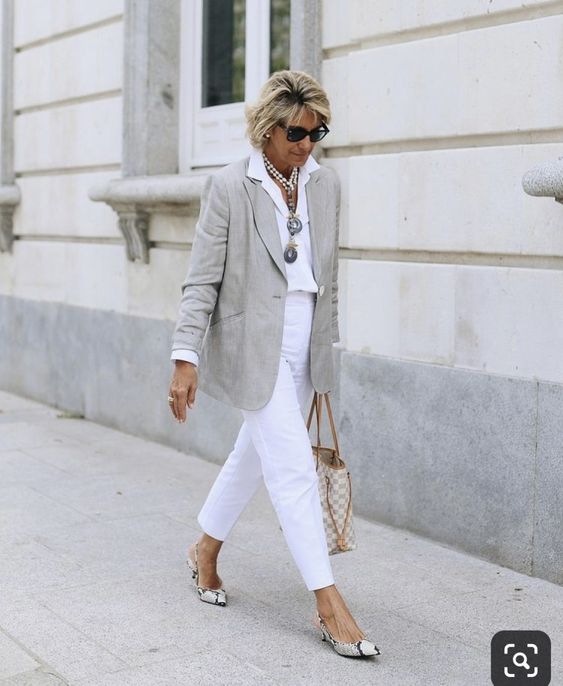 Mulher de 50 anos caminhando usando blazer e calça branca