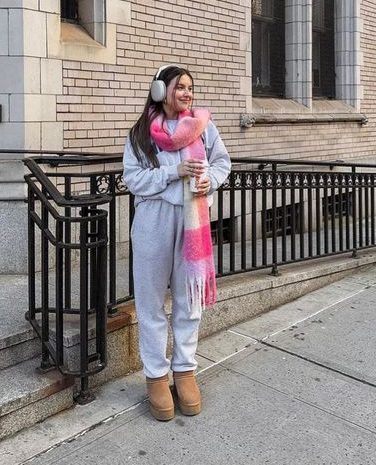 Mulher usando conjunto de moletom cinza claro. Ela está parada na frente de uma construção.