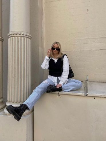 Mulher magra e loira de cabelos claros usando calça jeans, coelte e coturno preto