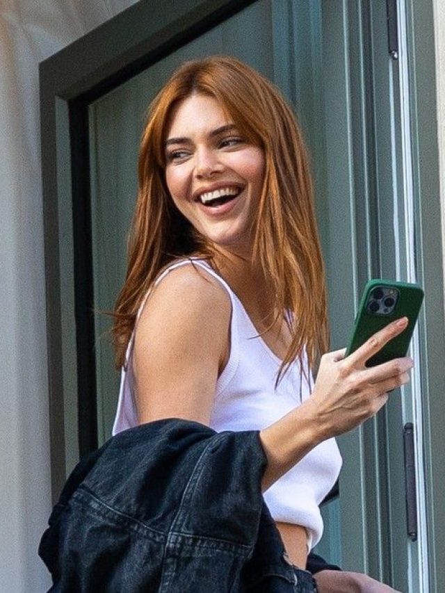 Kendall Jenner com regata branca, casaco no braço e cabelo médio ruivo com franja
