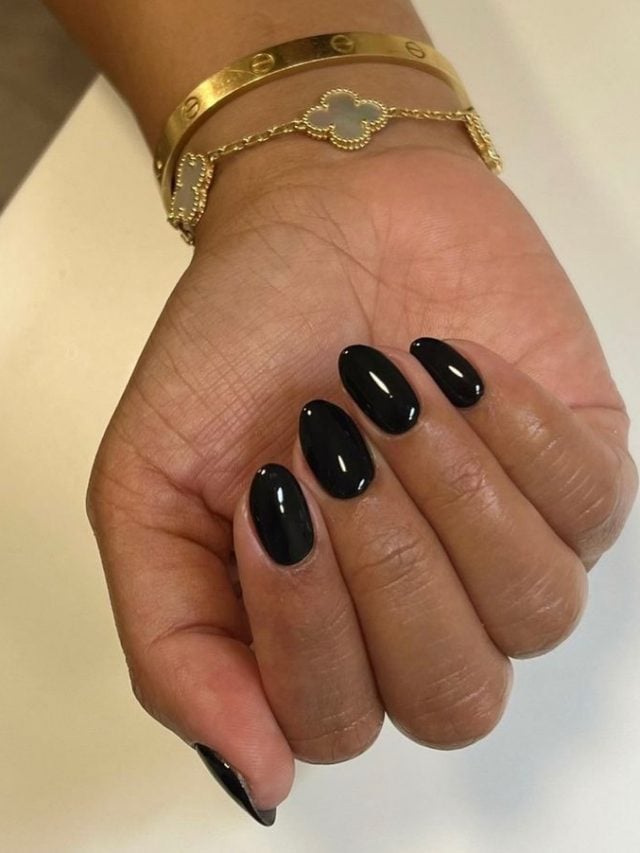 Mão branca curvada com unha amendoada preta e pulseiras