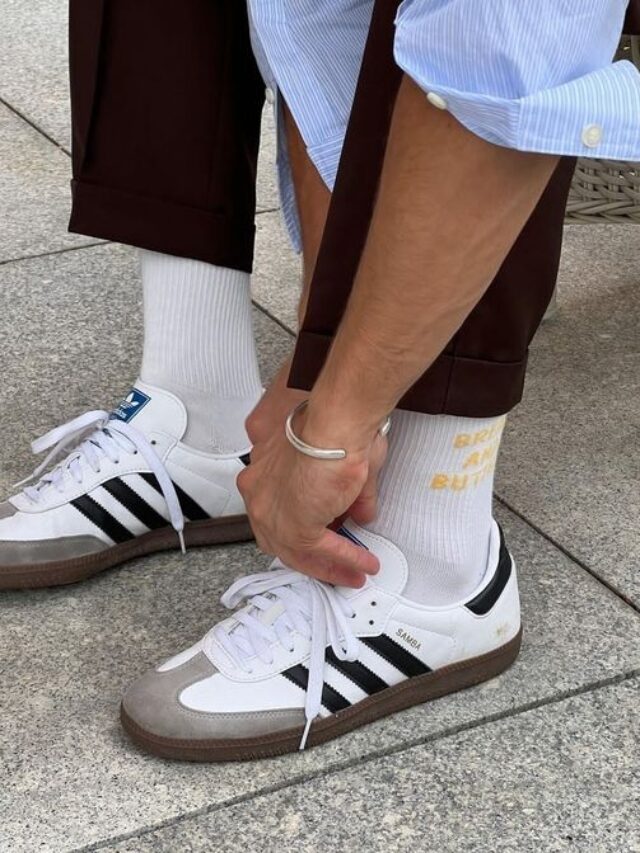 Foto de perna com calça marrom, meia branca e Adidas Samba