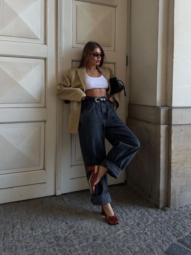 Mulher usando blazer longo aberto e top por baixo. Ela está usando jeans escuro e saltos
