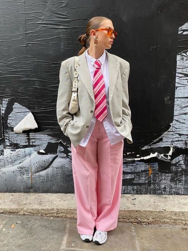Mulher branca usando calça rosa e blazer claro com gravata rosa