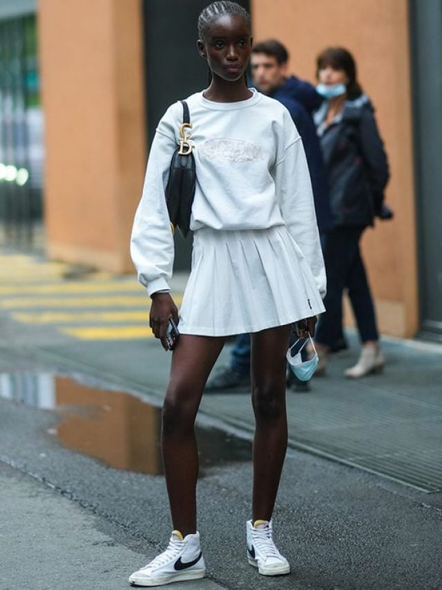 Mulher jovem e magra de pele escura. ela usa moletom, saia tenista e tenis nike