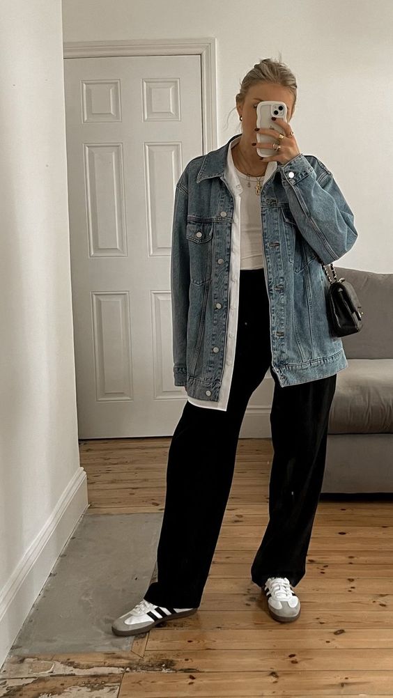 Mulher branca usando jaqueta jeans, calça preta e tênis