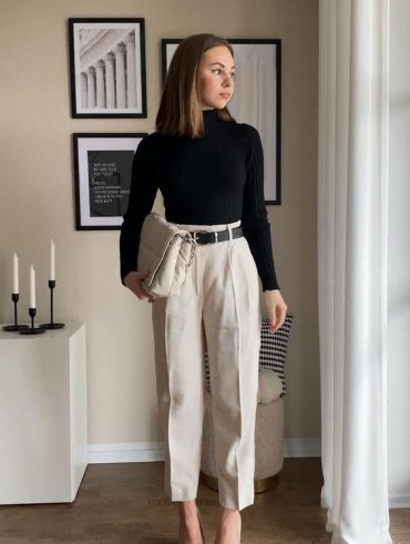 Mulher branca e de cabelos claros usando camiseta preta de manga longa, calça de alfaiataria e salto alto