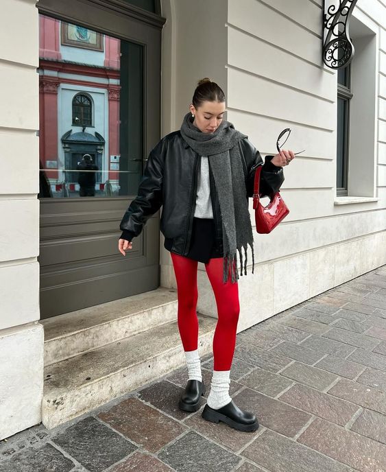 Moça usando casaco preto com cachecól de lã, shorts, meia-calça vermelha e sapato fechado.