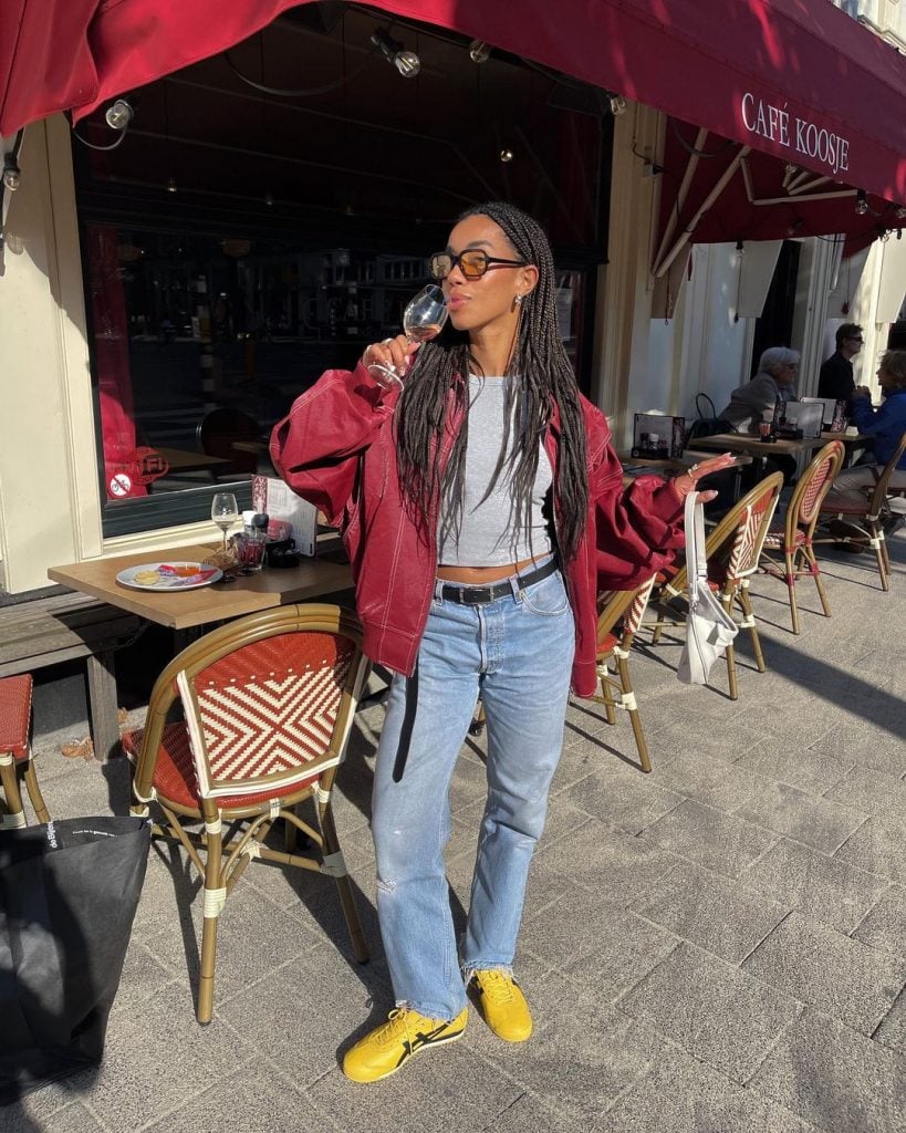 Amaka usando jaqueta de couro vermelha, baby-tee cinza, calça jeans reta e tênis Onisuka Tiger