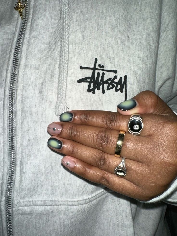Mão negra com anéis apoiada com aura nail e detalhes em prata metálico