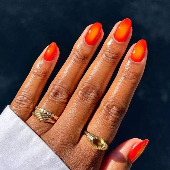 Mão negra com anéis dourados e aura nail laranja 