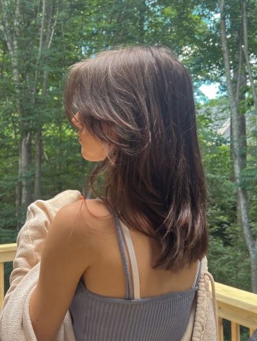 Mulher com cabelo médio e castanho, com franja no estilo curtain bangs