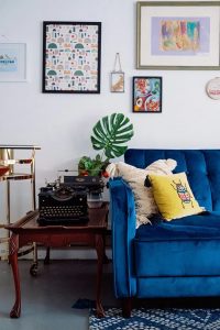 Sala com sofá azul de veludo, mesa de madeira e máquina de escrever
