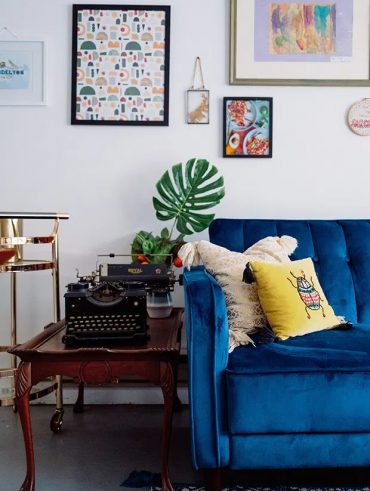 Sala com sofá azul de veludo, mesa de madeira e máquina de escrever