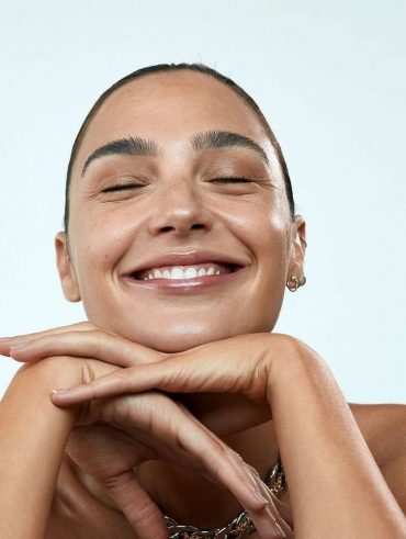 Mulher branca com as mãos apoiadas no queixo sorrindo