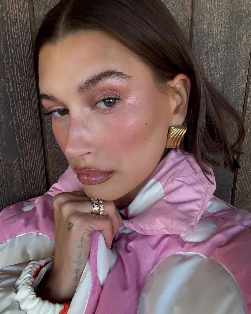 Hailey Bieber com roupa rosa e branca e maquiagem cintilante rosa