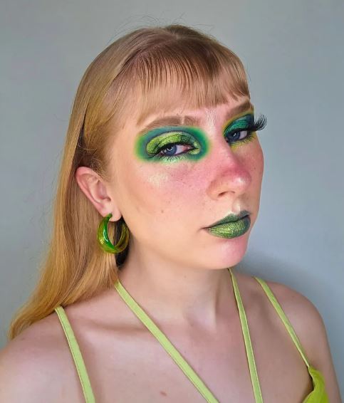 Mulher branca com blusa verde, cabelo ruivo com franja e maquiagem cromada na cor verde