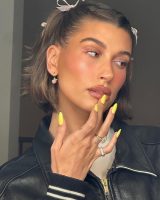 Hailey Bieber com delineado rosa, laços no cabelo e unha amarelo maracujá