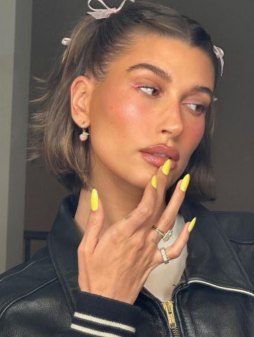 Hailey Bieber com delineado rosa, laços no cabelo e unha amarelo maracujá