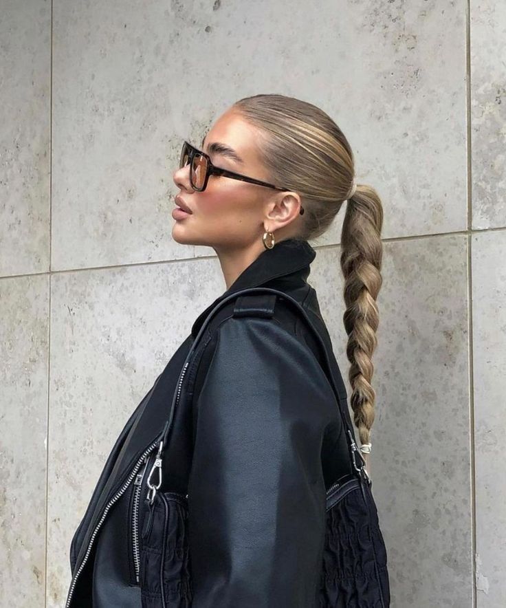 Mulher branca com look preto e cabelo loiro com rabo de cavalo trançado