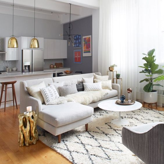 Sala e cozinha integradas com sofá claro e pendentes dourados