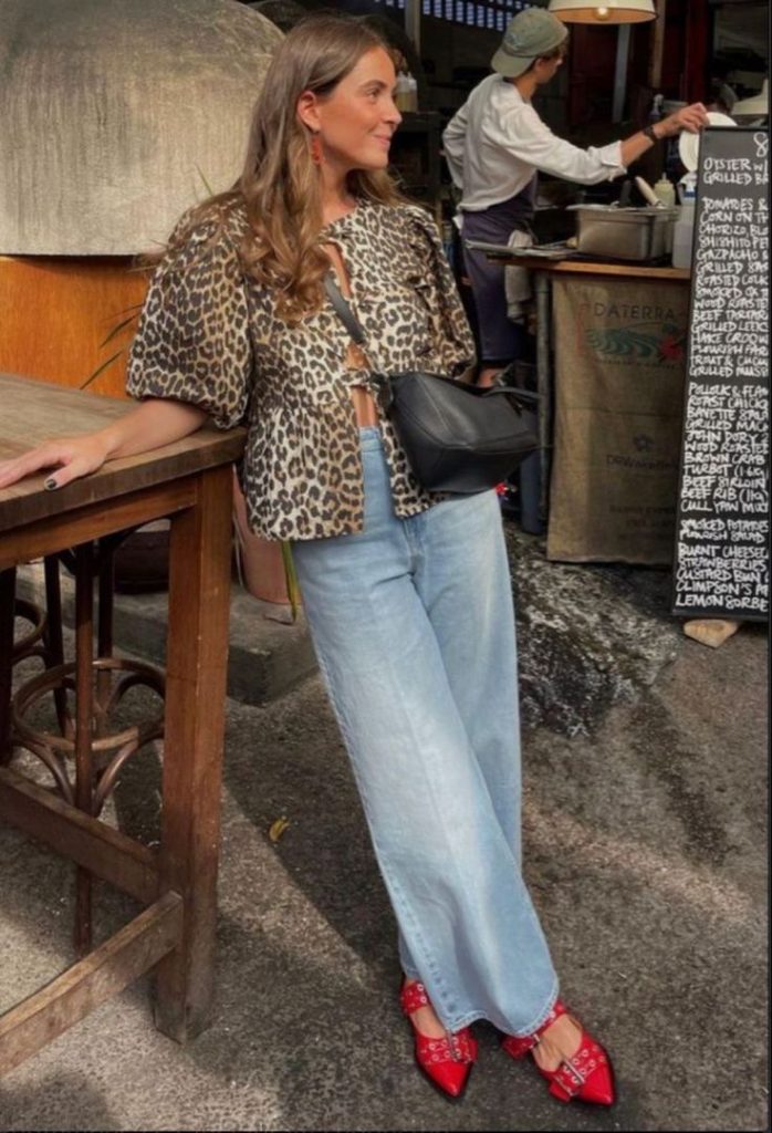 Mulher branca usando blusa de onça com top de laço, calça jeans e sapatilha Ganni