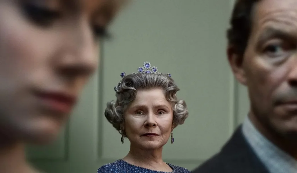 Dois personagens em segundo plano e a personagem que interpreta a Rainha Elizabeth de fundo 