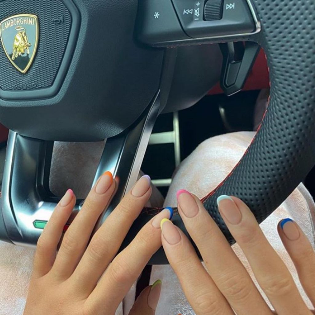 Mãos brancas abertas apoiadas no volante com a unha amendoada e francesinha colorida degradê