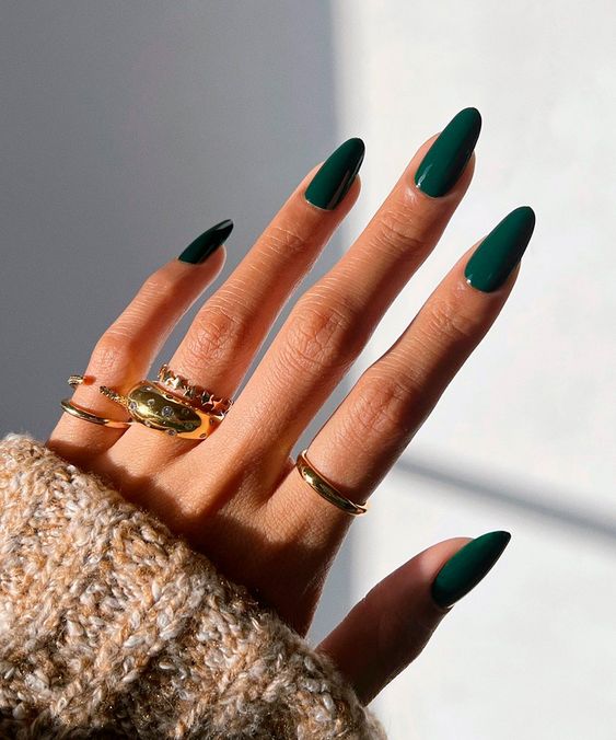 Mão branca com anéis dourados e unha amendoada verde esmeralda